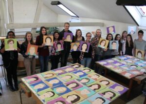 Das Bild zeigt eine Gruppe von Schülerinnen und Schülern, die ihre gemalten Portraits präsentieren