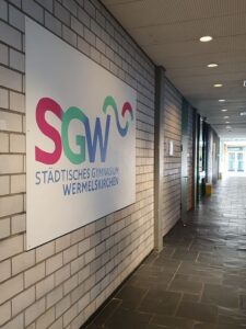 Das Bild zeigt das Logo des Gymnasiums Wermelskirchen gemalt im Schulflur hängend
