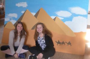 Das Bild zeigt zwei Schülerinnen, die vor ihrem gemalten Bild sitzen