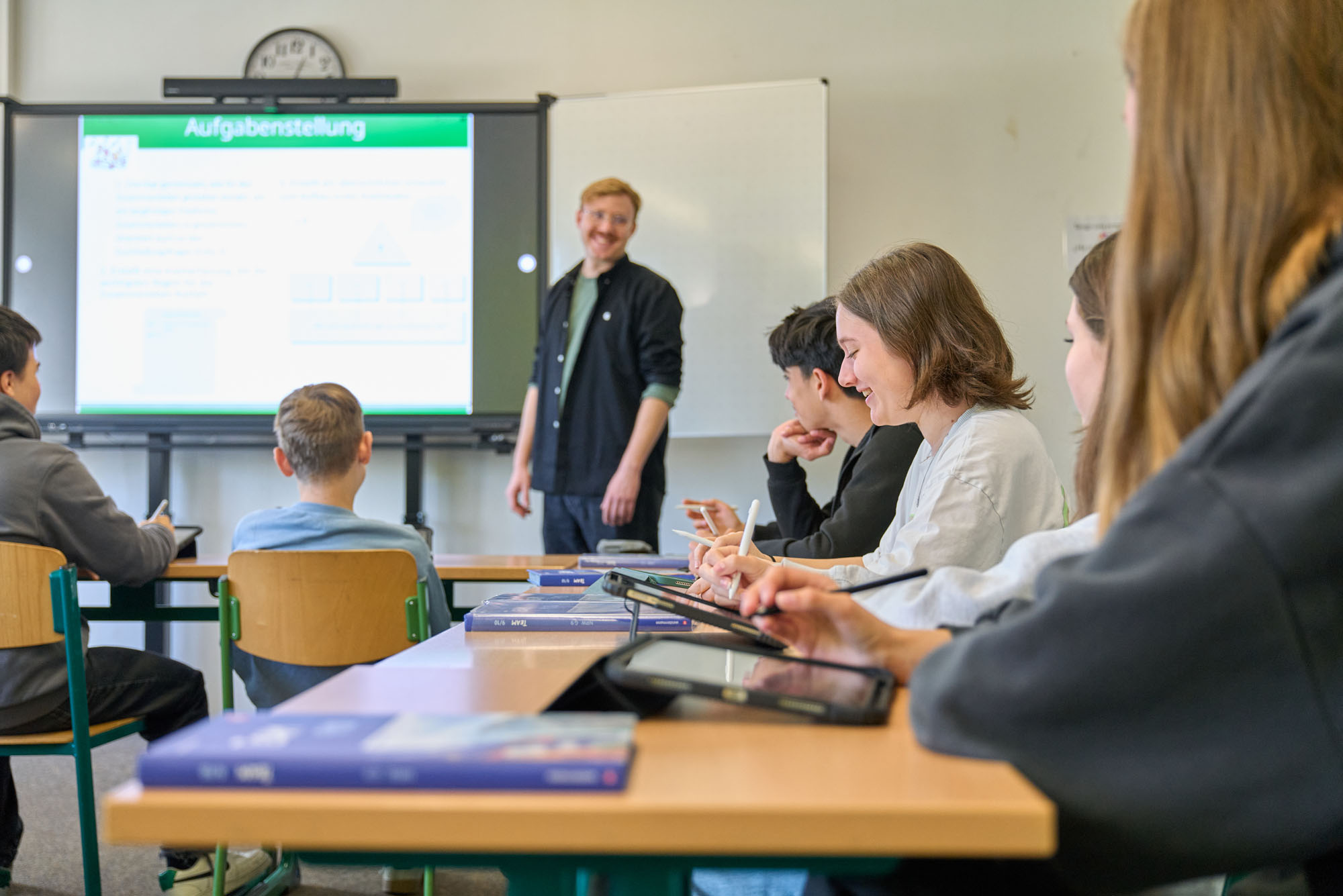 Das Bild zeigt eine Lernsituation im Klassenraum. Es sind ein Lehrer und einige Schüler zu sehen.